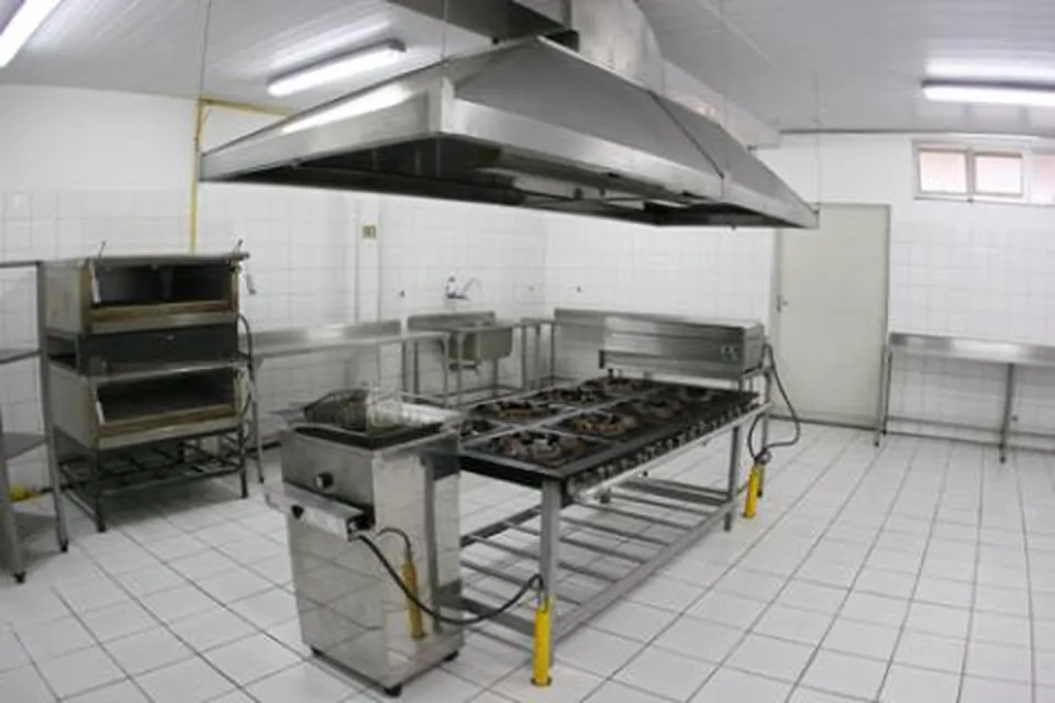 Cozinha profissional com coifa, mesas e equipamentos em inox